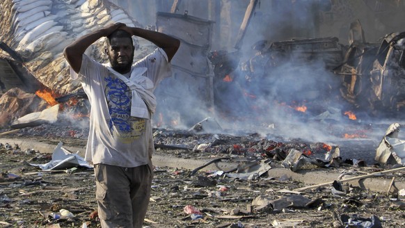 FILE -bIn this Saturday, Oct 14, 2017, file photo, a man walks past a dead body and destroyed buildings at the scene of a blast in the capital Mogadishu, Somalia. Somalia is marking the first annivers ...