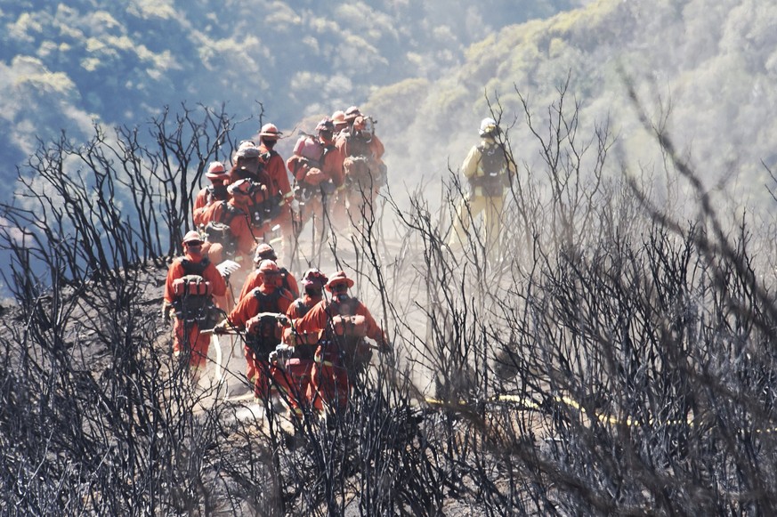 epa06399385 A handout photo made available by the Santa Barbara County Fire Department shows a CAL FIRE Inmate Firefighting Hand Crew hike through the charred landscape on their way to work east of Gi ...