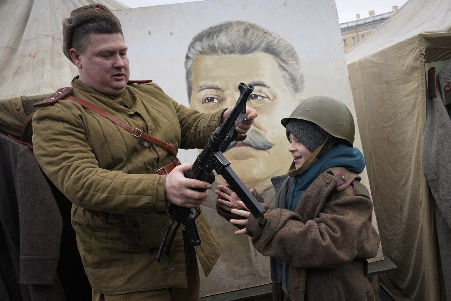 A member of a historic club wearing a World War II Soviet Army&#039;s uniform shows a gun to a boy near a portrait of Soviet dictator Josef Stalin at a military-historical exhibition at the Dvortsovay ...
