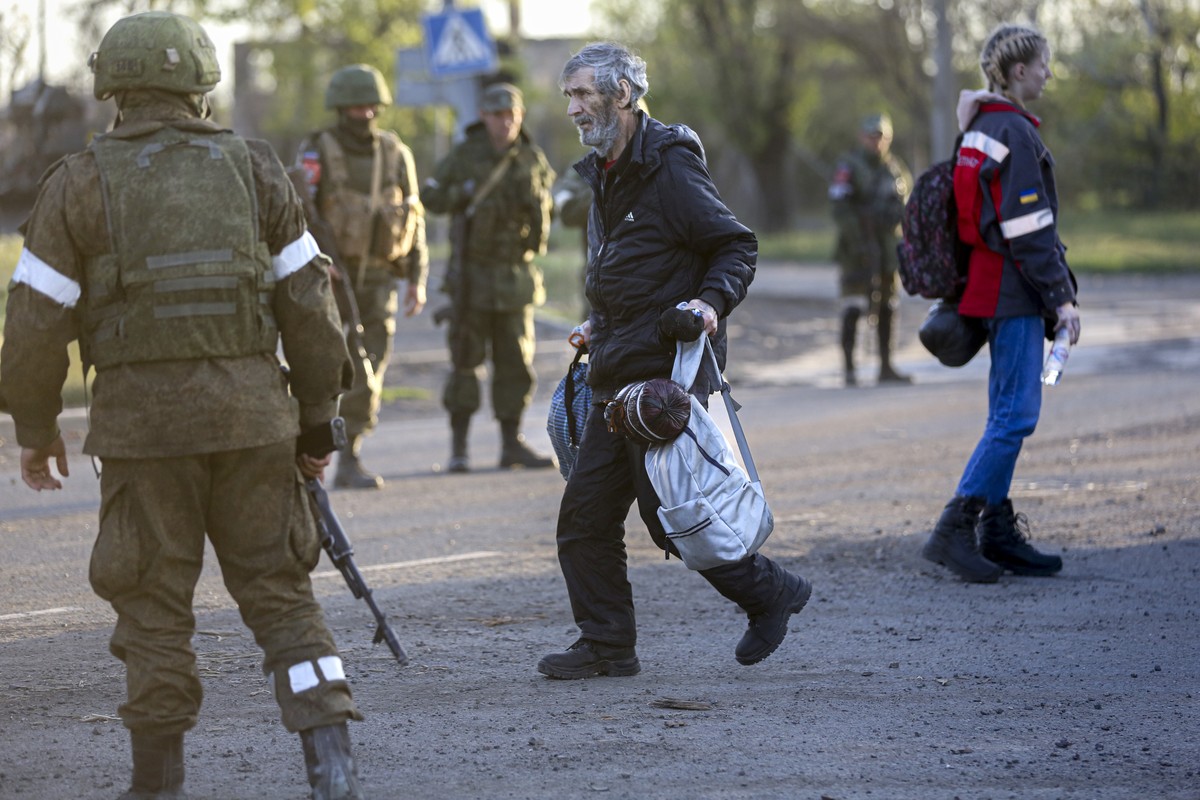 A man who left a shelter in the Metallurgical Combine Azovstal walks to a bus between servicemen of Russian Army and Donetsk People's Republic militia in Bezimenne village in Mariupol district, i ...