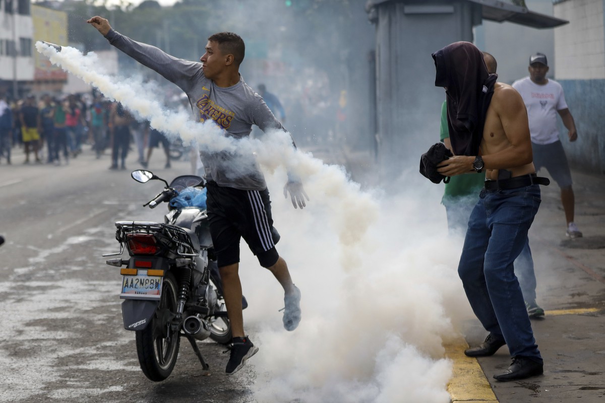 A protester throws a gas canister back at police during demonstrations against the official election results declaring President Nicolas Maduro's reelection, the day after the vote, in Caracas, V ...