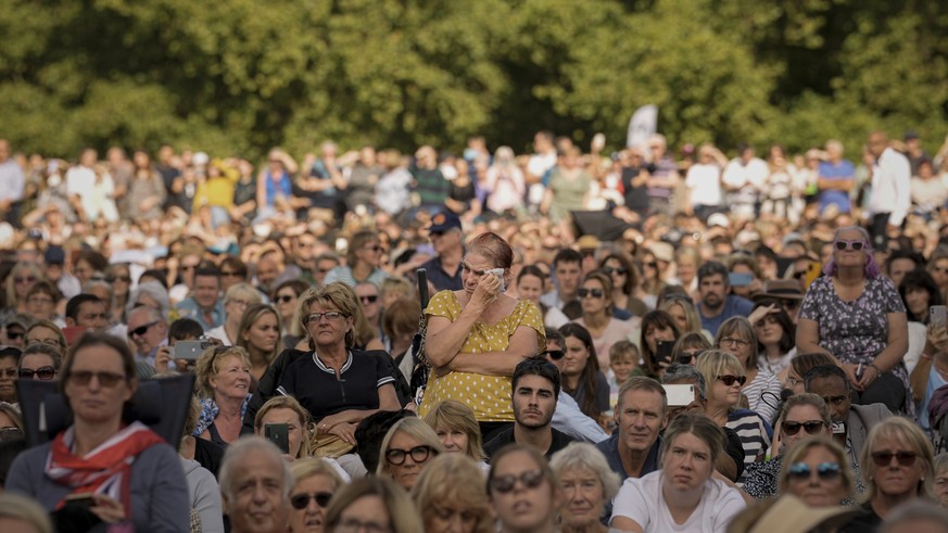 A woman wipes away tears as she joins people sitting in Hyde Park, London, Wednesday, Sept. 14, 2022 watching screens broadcasting the procession of the coffin of Queen Elizabeth II from Buckingham Pa ...