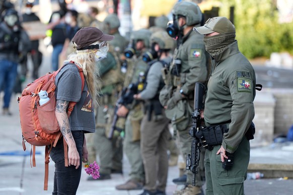 FILE - A woman stands off with a law enforcement officer wearing a Houston Field Office Special Response Team patch outside the U.S. Immigration and Customs (ICE) building during a protest Saturday, J ...