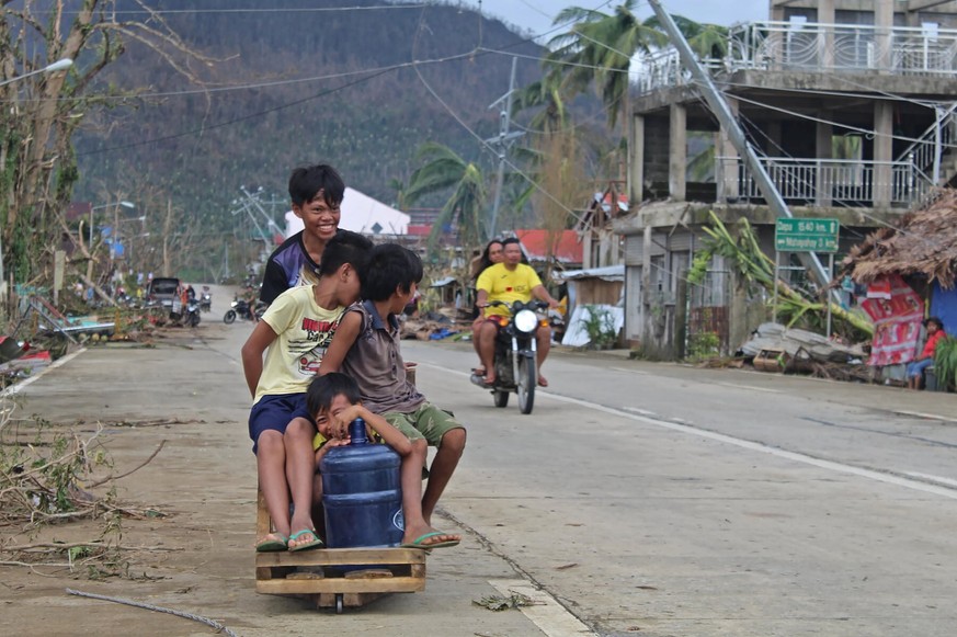 In this photo provided by the Philippine Coast Guard, children push a cart beside damaged homes due to Typhoon Rai in Surigao del Norte province, southern Philippines on Saturday, Dec. 18, 2021. The g ...