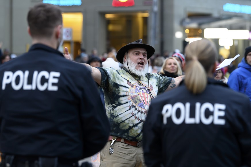 Ein Mann demonstriert gegen die Corona-Schutzmassnahmen des Bundes und wird von Polizisten ueberwacht, am Samstag, 19. Dezember 2020, auf dem Bundesplatz in Bern. (KEYSTONE/Anthony Anex)