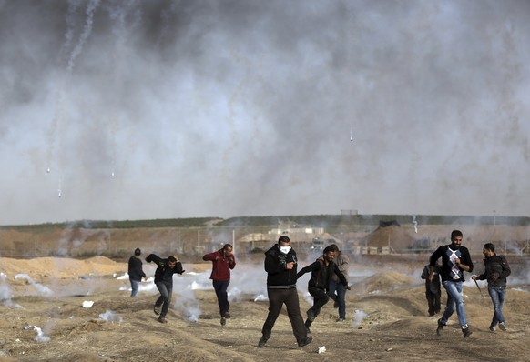 Palestinian protesters run for cover from teargas fired by Israeli troops during a protest at the Gaza Strip&#039;s border with Israel, Friday, April 13, 2018. (AP Photo/ Khalil Hamra)