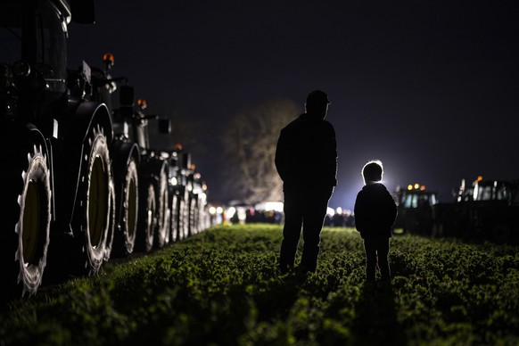 Ein Bauer hoert mit seinem Sohn den Ansprachen zu, als sich Vertreterinnen und Vertreter der Bauernbewegung mit ihren Traktoren zu einer Mahnwache treffen, um ihren Forderungen Nachdruck zu verleihen, ...