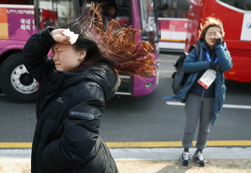 People block their faces from the wind as they leave buses at the 2018 Winter Olympics in Gangneung, South Korea, Wednesday, Feb. 14, 2018. Officials are asking spectators to evacuate the Olympic Park ...