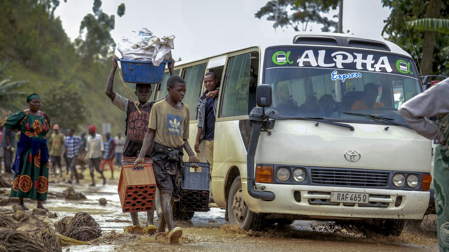 People walk and drive through flooding in Karongi district, Western Rwanda, Wednesday, May 3, 2023. Torrential rains caused flooding in western and northern Rwanda, killing more than 100 people, about...
