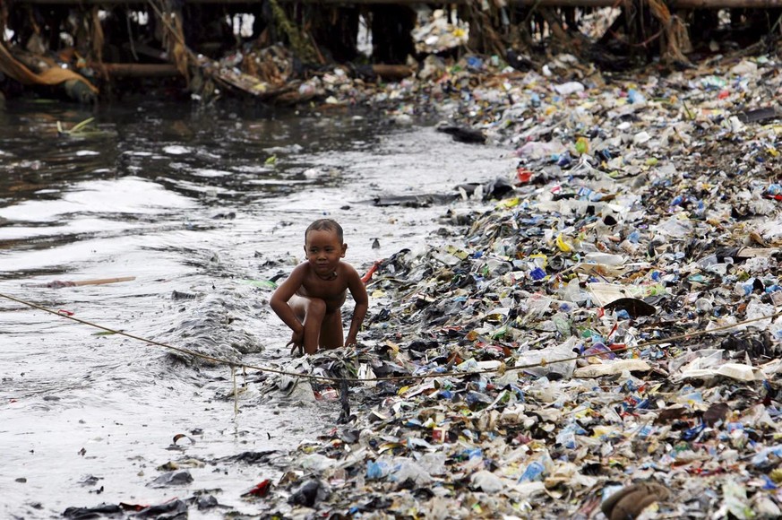 Ein kleiner Junge spielt an einem verschmutzen Strand von Jakarta, Indonesien.