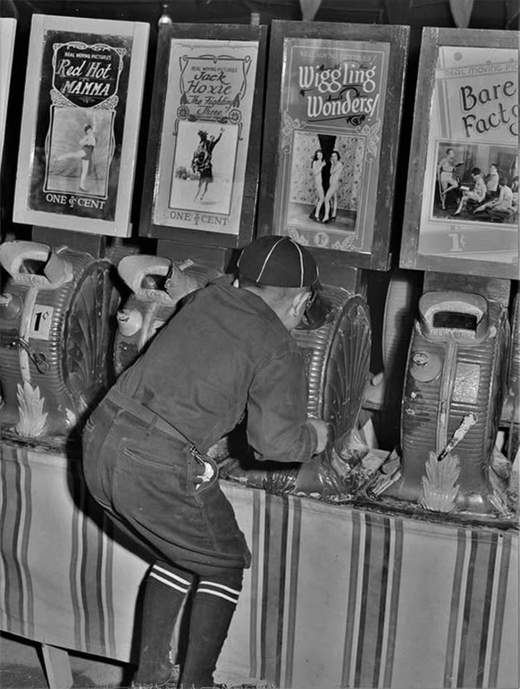A young man checking out a “Peep Show” at the penny arcade, 1940s