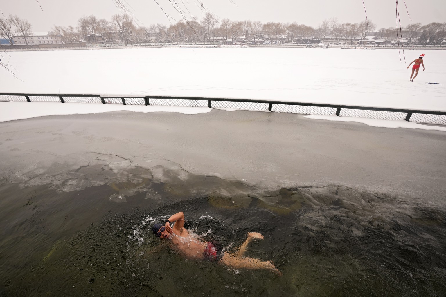 A man swims in the half-frozen water at the Shichahai Lake during a snow fall in Beijing, Sunday, Feb. 13, 2022. According to some of the local residents, swimming in the freezing water leads to healt ...