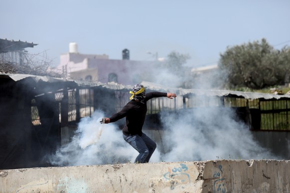 epa09863554 A Palestinian protester throws back a tear gas grenade during clashes after a demonstration against Israel&#039;s settlements on the lands of Kafr Qadoum village near the West Bank city of ...