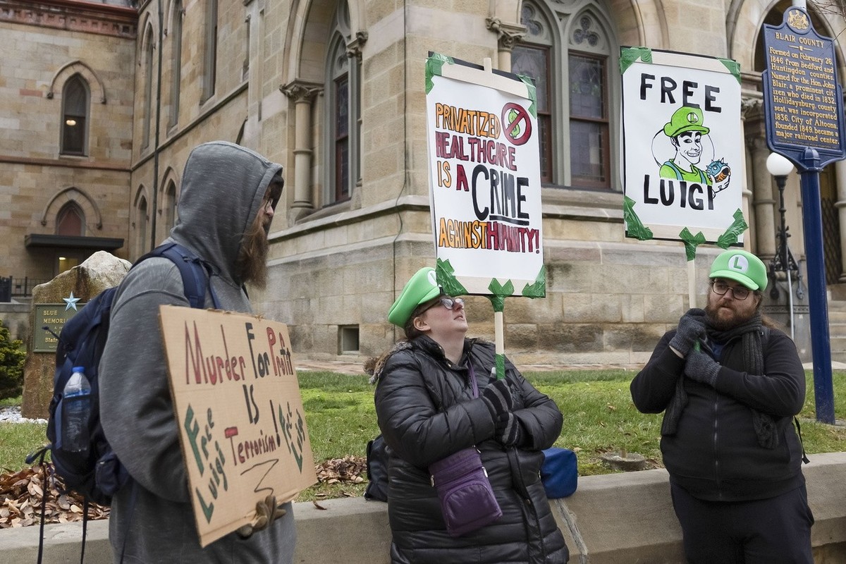 epa11785931 Adam Giesseman (L) and Ethan Merrill (R) stand with others holding protest signs outside of the Blair County Court House following a hearing for Luigi Mangione, who has been accused of kil ...