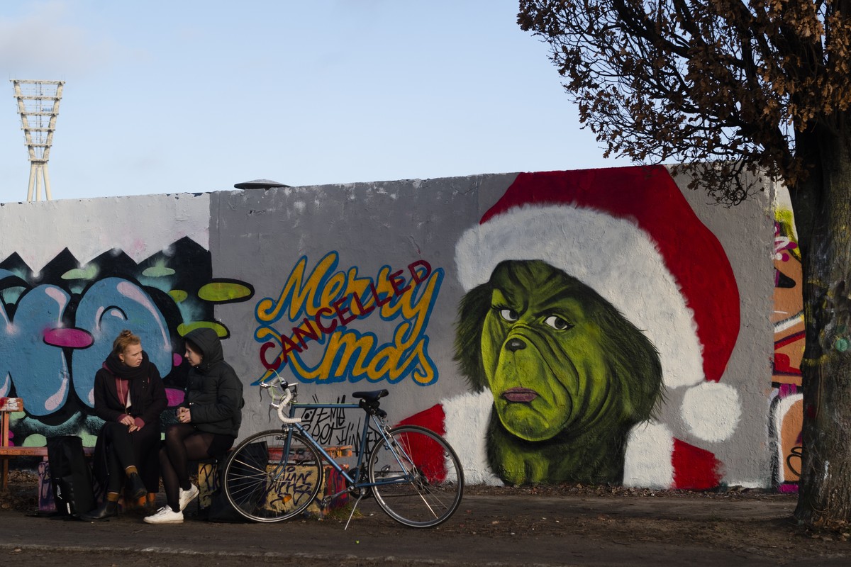 Two women sit on a bench in front of a graffiti by artist 'EME Freethinker' depicting the movie character 'The Grinch' and the slogan 'Merry Christmas - Cancelled' at the ...