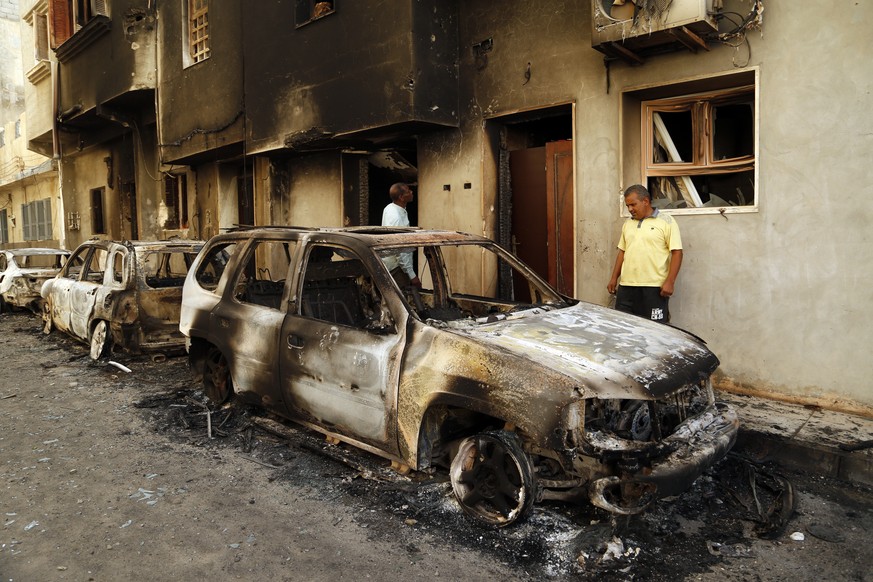 Men survey the remains of cars burned during clashes on a street in the Libyan capital of Tripoli, Sunday, August 28 2022. Deadly clashes broke out Saturday in Libya&#039;s capital between militias ba ...