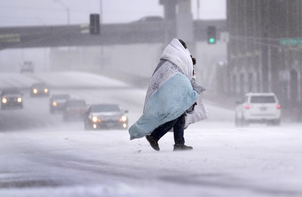 A person wrapped in a blanket crosses a snow-covered street Thursday, Dec. 22, 2022, in St. Louis. The frigid air is moving through the central United States to the east, with windchill advisories aff ...
