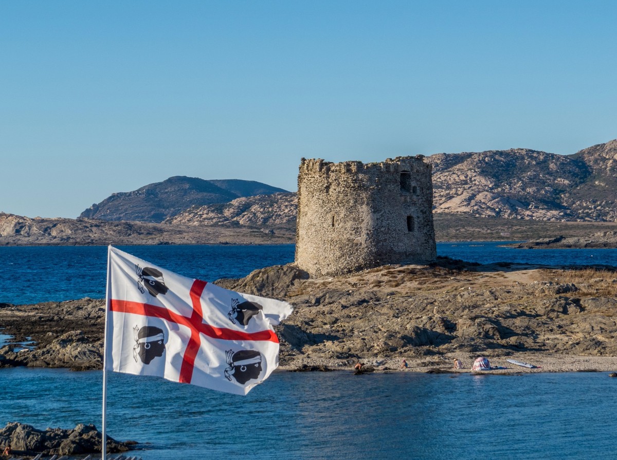 View of the famous La Pelosa Beach with the Sardinian flag and the landmark 16th century Watchtower (Italian: Torre della Pelosa) in the background.