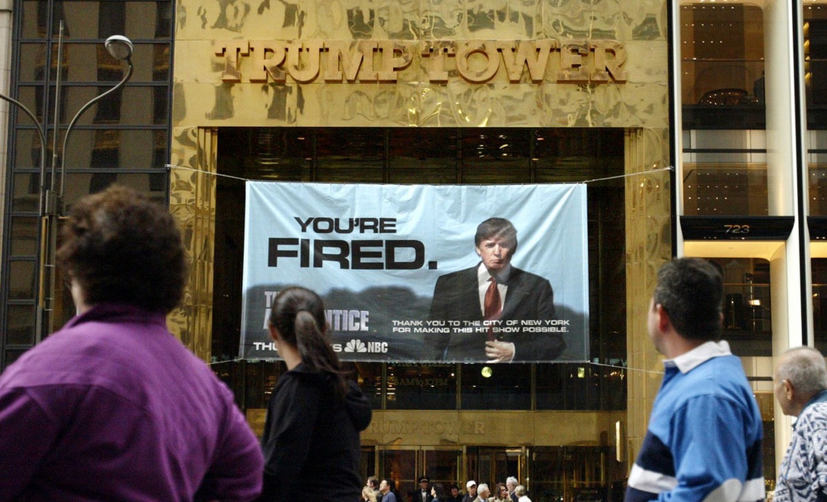 In this March 27, 2004 photo, passersby look at a sign from Donald Trump's television show, "The Apprentice," hung on the Trump Tower in New York. The skyline shimmers, the music pulses ...