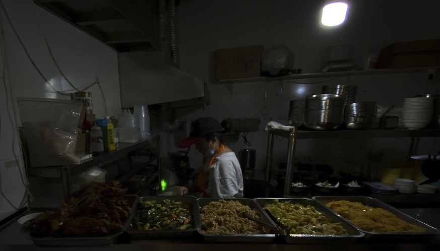 A woman uses a light bulb powered by portable battery as she prepares dishes in an earlier morning at a restaurant during a blackout in Shenyang in northeastern China's Liaoning Province, Wednesd ...