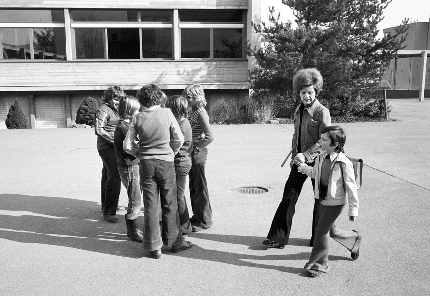 Waehrend aeltere Schueler auf dem Pausenplatz eines Schulhauses in Schwerzenbach miteinander sprechen, bringt eine Mutter ihr Kind am 14. April 1975 am ersten Schultag zur Schule. (KEYSTONE/Str)