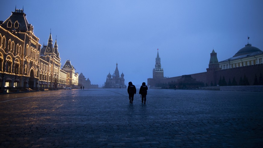 Two police officers patrol an almost empty Red Square, with St. Basil's Cathedral in the middle and the Spasskaya Tower and the Kremlin Wall, right at the time when it is usually very busy in Moscow, Ru...