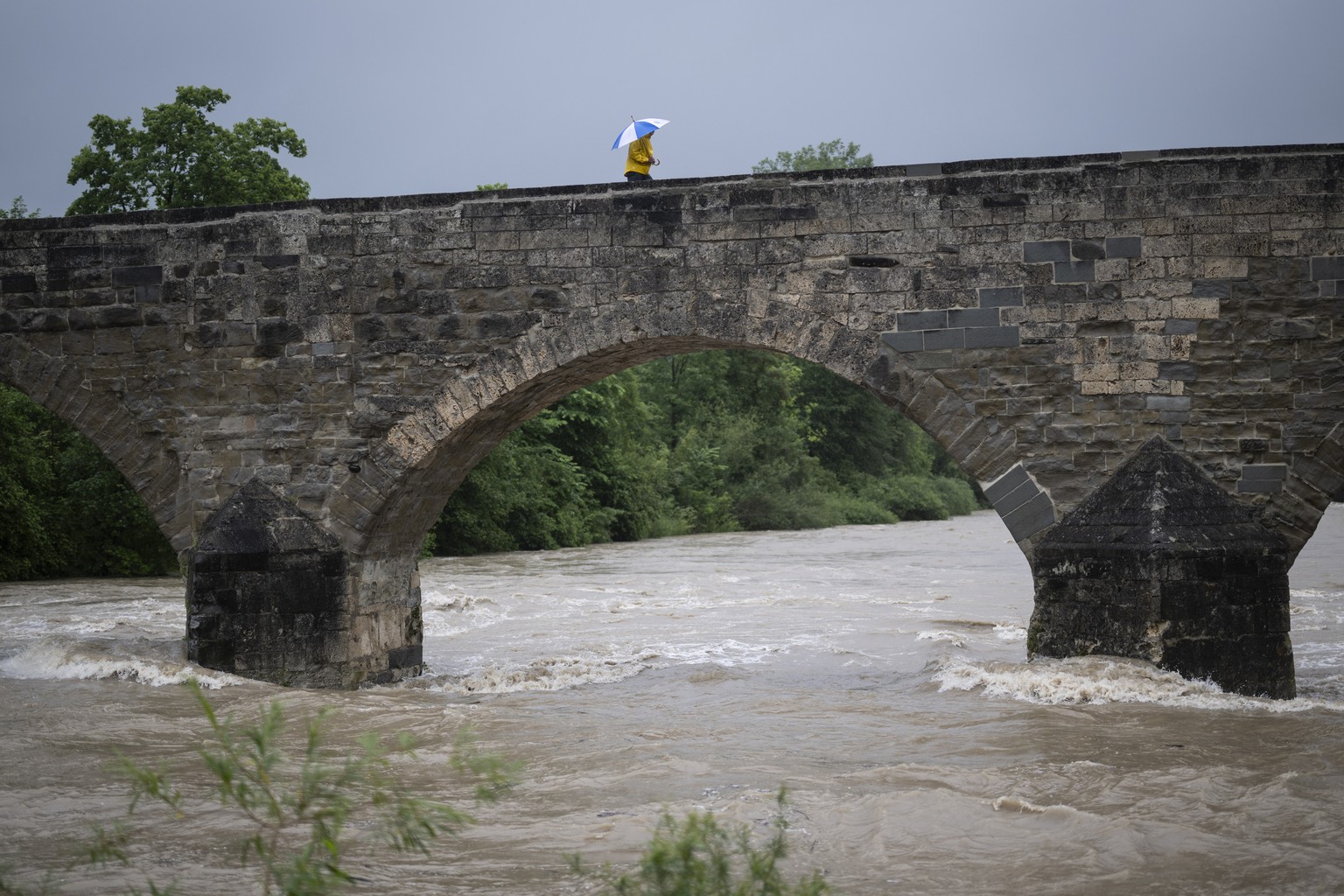 Ein Spaziergaenger mit Regenschirm geht ueber die alte Thurbruecke bei hohem Pegelstand, aufgenommen am Freitag, 31. Mai 2024, in Bischofszell. Mehrere Gewaesser in der Ostschweiz fuehren wegen der st ...