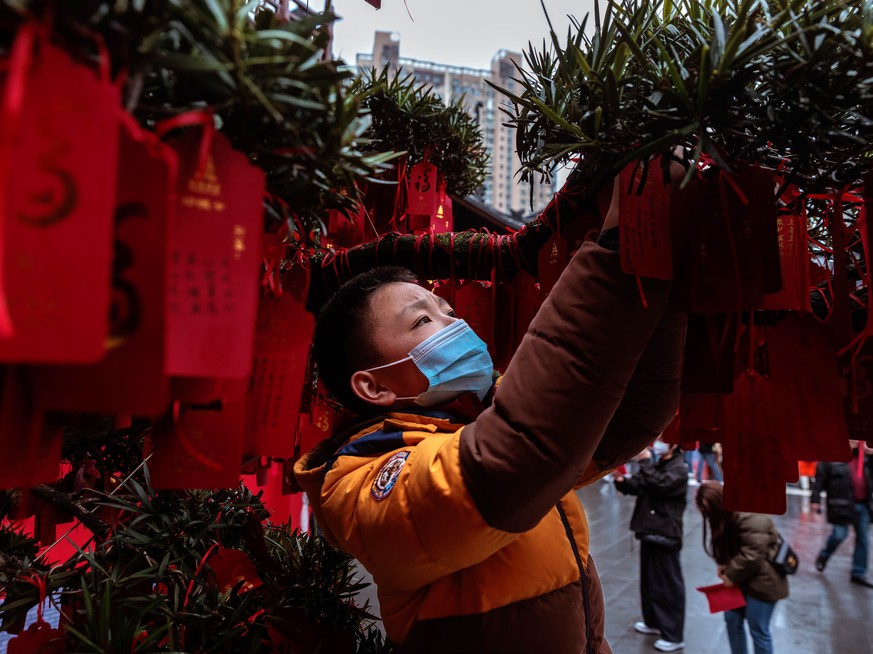 epa10422475 A boy hangs prayers on the wishing and money tree on the first day of the Chinese Lunar New Year in the Jade Buddha Temple, in Shanghai, China, 22 January 2023. Chinese New Year, also know ...