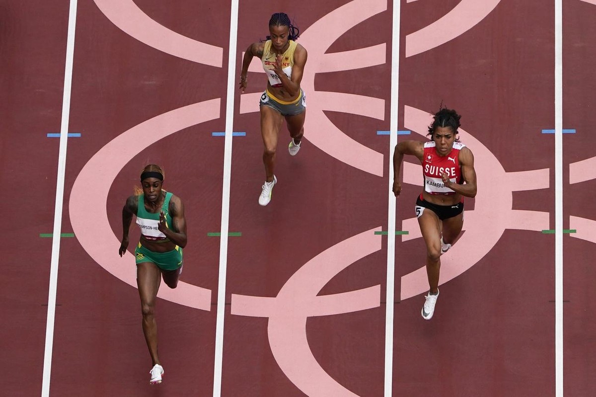Elaine Thompson-Herah, of Jamaica, Tatjana Pinto, of Germany, and nd Mujinga Kambundji, of Switzerland, compete during the first round of the women's 100-meter the 2020 Summer Olympics, Friday, J ...