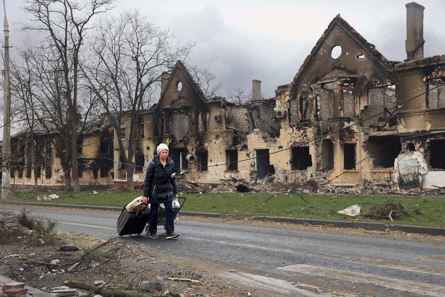 FILE - A woman pulls her bags past houses damaged during fighting in eastern Mariupol, Ukraine, Friday, April 8, 2022. Ukraine says it is investigating a claim that a poisonous substance was dropped o ...