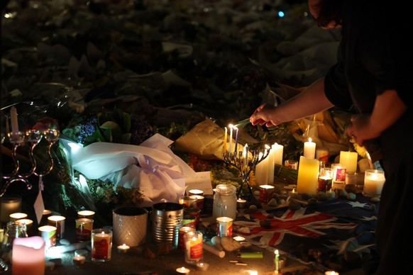 epa12596290 A mourner lights a candle at makeshift memorial at Bondi Beach in Sydney, New South Wales, Australia, 16 December 2025. Australia is in mourning following an attack on the Jewish community ...