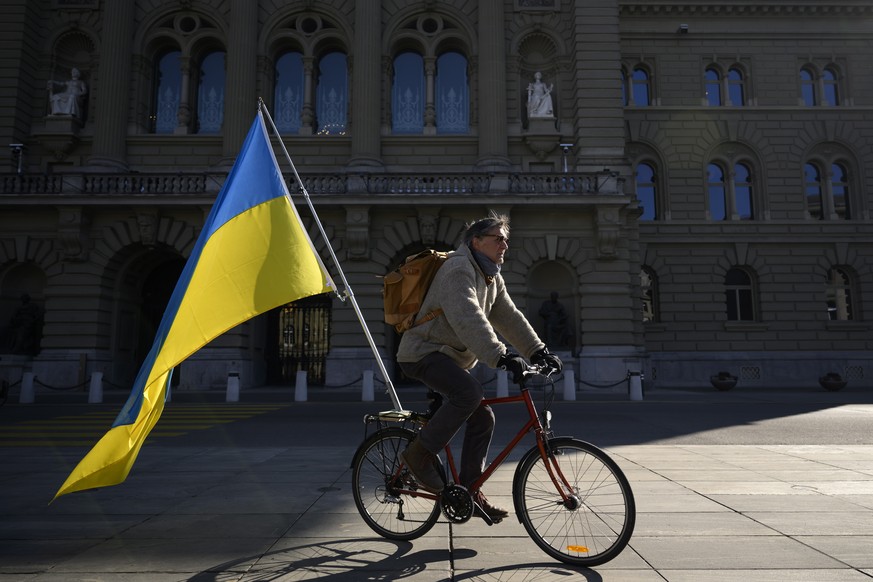 epa09803864 A man on a bicycle with a Ukrainian flag in a demonstration against the Russian invasion of Ukraine, in front of the Swiss parliament building, at the Bundesplatz square in Bern, Switzerla ...