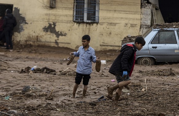 Youngster walk along a street covered of mud during floods after heavy rains in Sanliurfa, Turkey, Thursday, March 16, 2023. Rescue teams on Thursday retrieved two more bodies after a floods struck tw ...
