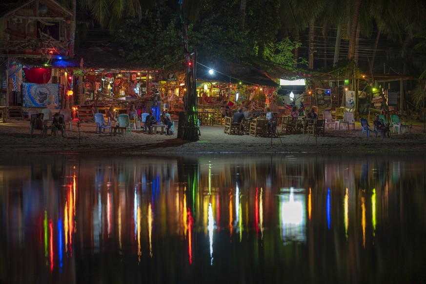 Beach bar, coconut palm trees, sea water and night club is reflected in seawater at tropical island Koh Phangan, Thailand, KOH PHANGAN, THAILAND - MAY 03, 2019 : Beach bar, coconut palm trees, sea wat ...