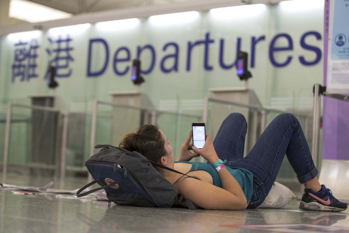 A traveler leans on her bag while browsing her smartphone at the departure hall of the Hong Kong International airport on Monday, Aug. 12, 2019. One of the world's busiest airports canceled all f ...