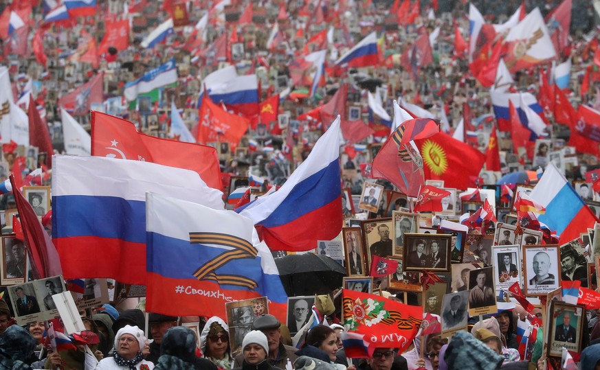 epa09936226 A person carries a flag with the letter Z next to people holding portraits of their relatives who fought World War II, during an Immortal Regiment memorial in Moscow, Russia, 09 May 2022.  ...
