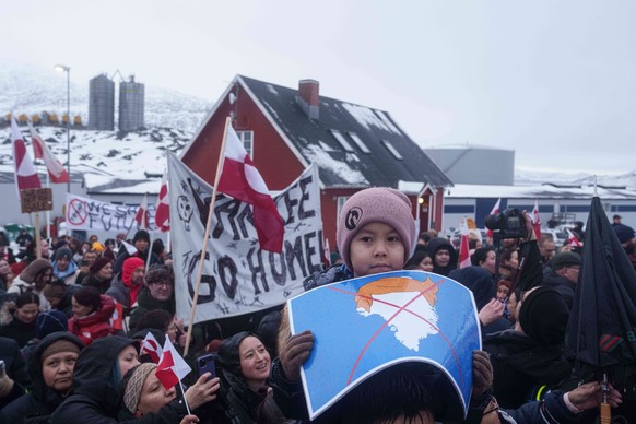 A boy holds a crossed out map of Greenland topped by a hairpiece symbolizing U.S. President Donald Trump, during a protest against Trump's policy towards Greenland in front of the US consulate in ...
