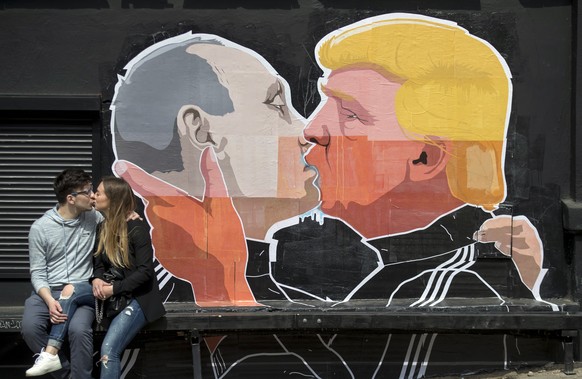 A couple kisses in front of graffiti depicting Russian President Vladimir Putin, left, and Republican presidential candidate Donald Trump, on the walls of a bar in the old town in Vilnius, Lithuania, ...