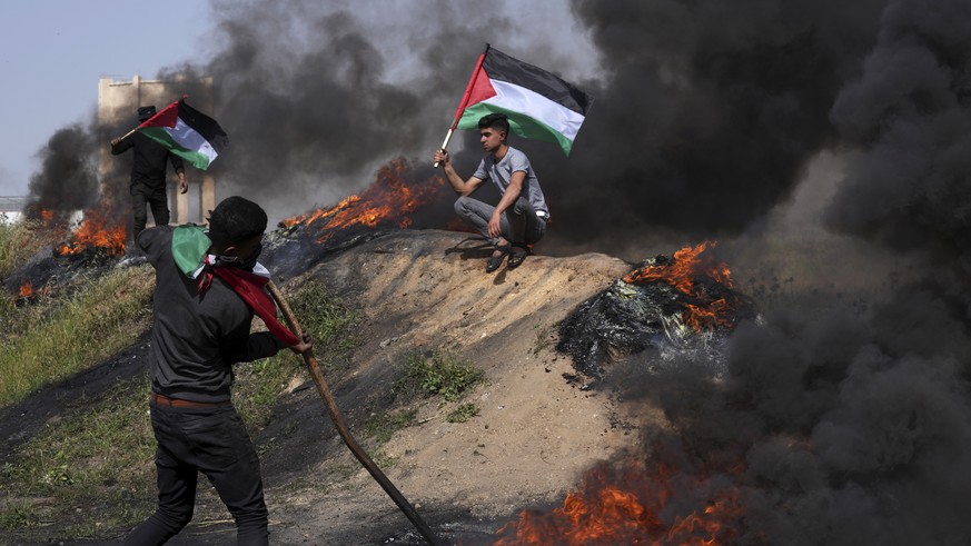 Palestinians burn tires and wave the national flag during a protest against an Israeli police raid of the Al-Aqsa Mosque compound in Jerusalem&#039;s Old City early Wednesday, along the border fence w ...