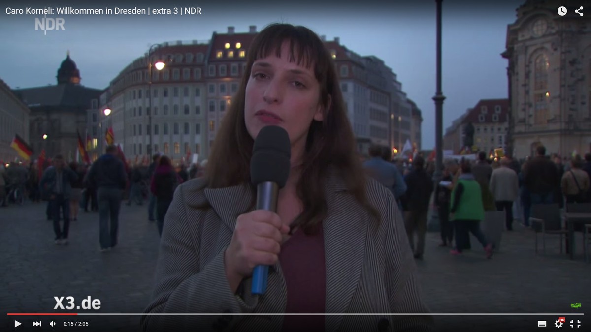 Vorne: Extra 3-Moderatorin, im Hintergrund: Traumatisierte Masse.