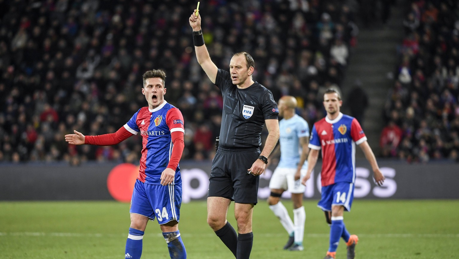 epa06522346 Referee Jonas Eriksson from Sweden (C) shows the yellow card to Basel&#039;s Taulant Xhaka (L) during the UEFA Champions League round of 16 first leg soccer match between FC Basel and Manc ...
