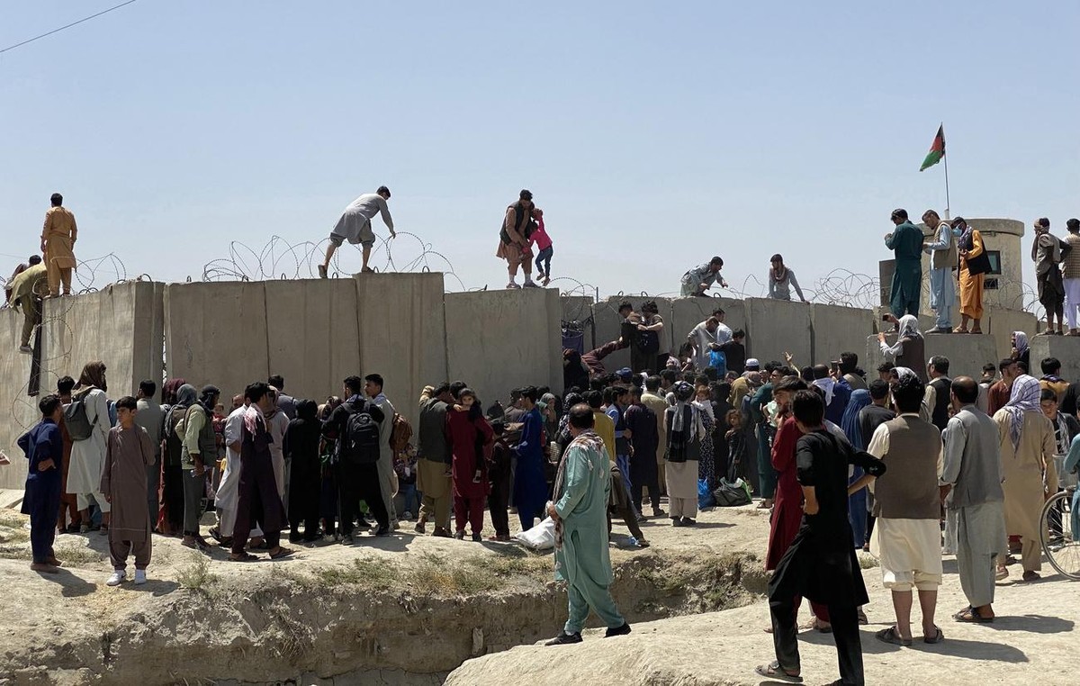 epa09416177 People struggle to cross the boundary wall of Hamid Karzai International Airport to flee the country after rumors that foreign countries are evacuating people even without visas, after Tal ...