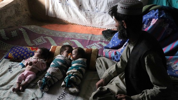 epa09625453 Ehsanullah, a father or newborn triplets sons sit next to his babies at his home in Kandahar, Afghanistan, 06 December 2021. Ehsanullahl said he was grateful to Allah for blessing him with ...