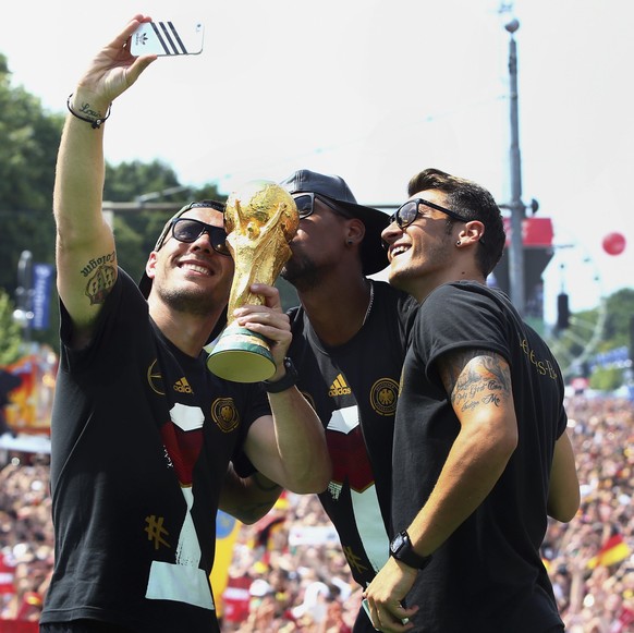 Germany&#039;s Lukas Podolski, Jerome Boateng and Mesut Oezil (L-R) pose for a &#039;selfie&#039; with the World Cup trophy during celebrations to mark the team&#039;s 2014 Brazil World Cup victory, a ...