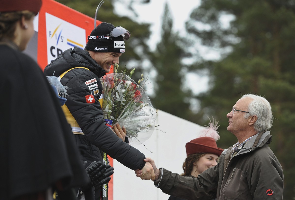 Swiss Dario Cologna, left, shakes hands from the winner's stand with Sweden's King Carl XVI Gustaf, right, after Cologna's victory in the men's 15km mass start World Cup ski race i ...