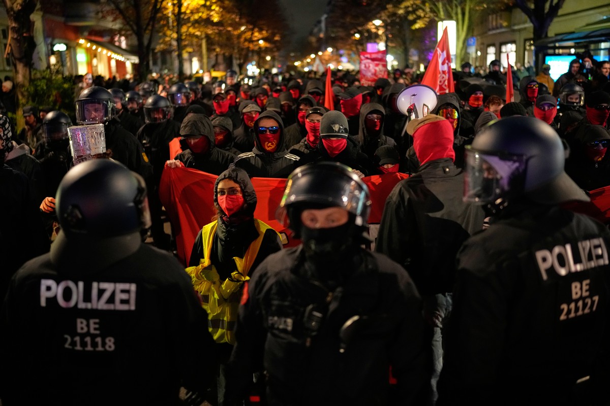 Police officers walk in front of demonstrators with covered faces during a protest under the slogan "Gen Z Takes Care of It" in Berlin, Germany, Saturday, Oct. 31, 2026. (AP Photo/Ebrahim No ...