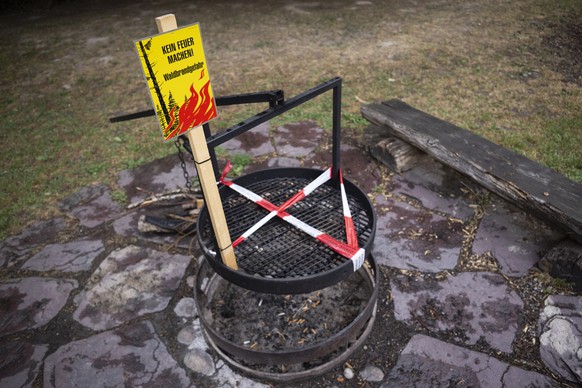 Eine Grillstelle in einem Schweizer Wald ist gesperrt. Ein gelbes Warnschild weist auf das absolute Feuerverbot hin, und ein rot-weisses Absperrband blockiert den Zugang zum Grillrost,, nahe Recherswi ...