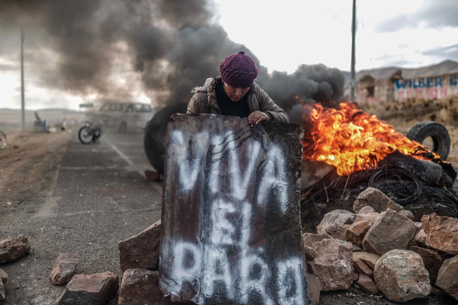 epa10394494 A man stands at a burning barricade as the community of La Estrella between Cusco and Juliaca block the roads in the vicinity of the Juliaca airport in Juliaca, Peru, 07 January 2022. Prot ...