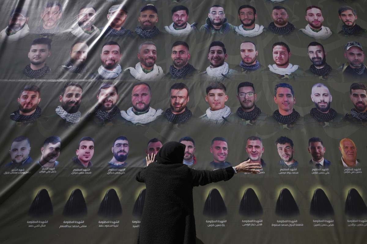 A woman reacts next to pictures of Hezbollah fighters as mourners march to bury the bodies of nearly 100 Lebanese people killed during the war between Israel and Hezbollah in the largest mass funeral  ...