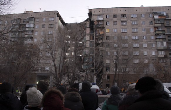 epa07254870 People watch as Russian rescue workers remove debris after a gas explosion in a apartment building in the city of Magnitogorsk, Chelyabinsk region, Russia, 31 December 2018. The explosion  ...